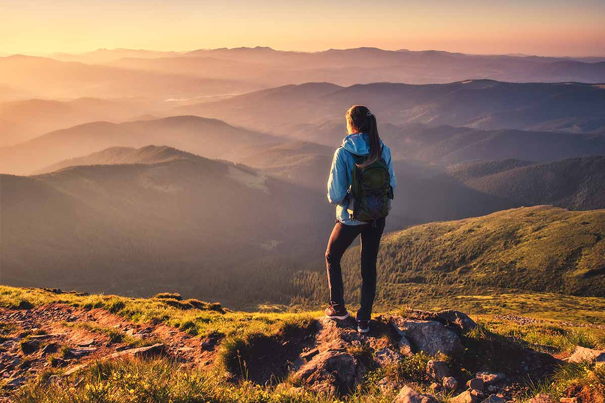 Robo Advisor Preise Wanderin steht auf dem Berggipfel und blickt auf die umliegenden Bergketten