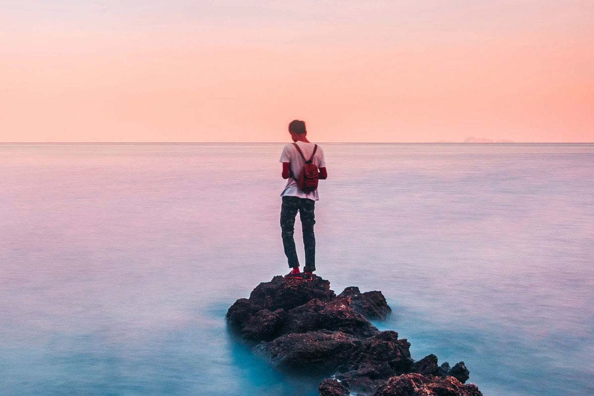 Digitale Geldanlage Mann steht auf einem Felsen im Meer und blickt in die Ferne