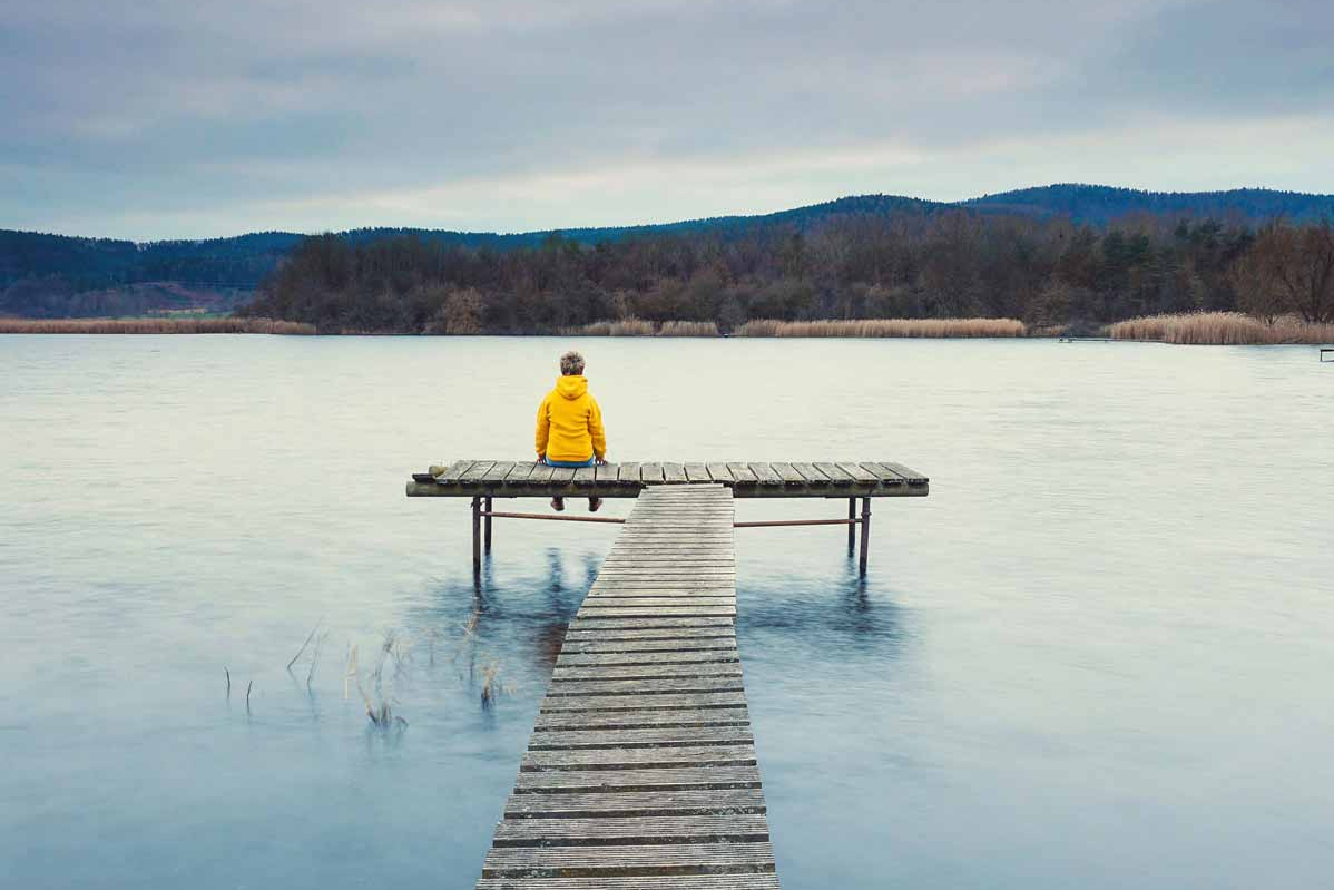 Gemanagte ETF-Portfolios Person sitzt auf einem Steg und blickt auf den See